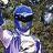 Pixelated static image of a figure with blue hair and dark sunglasses against a blurred greenish background.