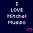 Dark blue background with repeated white text "I LOVE Mitchel Musso" and pink pixelated hearts, partially cropped at bottom right.