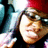 A person wearing a red beanie and dark glasses with a hand raised in a waving gesture, displayed in a
