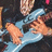 Pixelated image of a person in light blue clothing with hands near the face against dark background.