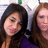 Two people with long hair pose closely together, one in a purple top against a light background.