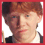 Pixelated image of a person with red hair wearing dark clothing and a white collar, showing partial views including the head, shoulder, and chest emblem.