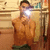 A person in a brown shirt and dark pants takes a mirror selfie with a bright flash, standing before a shelf of items.