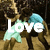 Pixelated image with large white text 'Love' overlaid on a background featuring two figures in brown and blue tones.