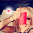 A pixelated image shows a person with light brown hair holding a red rectangular object near their face, with a heart symbol in the background.