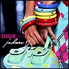 A close-up of hands holding a light green handbag with multiple compartments, adorned with colorful stacked bracelets and a patterned garment.