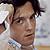 Pixelated close-up of a person with dark hair and light skin wearing a white collared shirt against a blurred background.