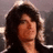 Pixelated static image of a person with long dark hair and light skin, wearing a dark top against a muted gray background.