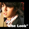 A close-up of a person with dark tousled hair wearing a dark jacket over a light pink striped shirt and a patterned neckerchief, with text reading "The Look" at the bottom.