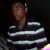 Pixelated image of a person with short brown hair wearing a dark blue shirt with white horizontal stripes, arms crossed against a black background.