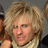 Pixelated close-up of a person with voluminous curly blonde hair, light skin tone, and visible facial features including eyes, nose, mouth, and ear.