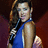 Pixelated image of a person with long dark hair wearing a blue sleeveless top, holding a microphone against a gradient background.