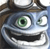 Pixelated cartoon face with large green eyes, wide open mouth showing teeth, and a brown hat-like shape on top.
