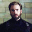 Static 64x64 pixel icon showing a man with short brown hair and beard wearing a black turtleneck sweater against a blurred greenish background.