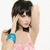 Pixelated image of a person with short dark hair wearing a pink top and blue accessory, raising one arm near their head.