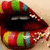 Pixelated close-up of a mouth with dark lips, visible teeth, and colorful striped patterns on the upper lip.