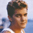 Pixelated image of a person with short brown hair wearing a white sleeveless top against a light blue background, accompanied by pink pixelated text and symbols on black.