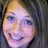 Pixelated close-up of a smiling person with light brown hair and blue eyes, wearing a dark top against a dark background.