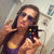 A pixelated image shows a person with long dark hair wearing sunglasses and a yellow and purple top, holding a small device with colored buttons.