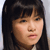 Pixelated close-up of a person with long dark hair and bangs, light skin, and a neutral expression against a light background.