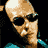 Pixelated static image of a bald man with dark sunglasses and teal clothing against black background.