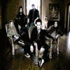 A group of people in formal attire pose in a dimly lit room with framed artwork on the wall.