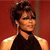 Pixelated image of a person with short dark hair wearing a sleeveless dark top against a solid red background.