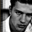 Black-and-white pixelated static image of a person's face with visible hair and partial shoulder, rendered in low-resolution grayscale with dithering effects on the background.