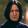 Static image of a person with shoulder-length dark hair wearing a dark turtleneck and purple-accented garment against a blurred background.