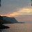 Pixelated static image of a coastal landscape at sunset with a dark rocky outcrop on the left and a gradient sky transitioning from orange to gray.