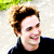 Pixelated static image of a person with light brown curly hair, wearing dark clothing against a bright background with green foliage.