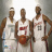 Three basketball players in white jerseys stand side-by-side, one holding a brown basketball.