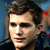 Pixelated close-up of a person with light brown hair, wearing a dark jacket against a blue background with red and purple accents.