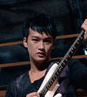 A person holding a white electric guitar with dark fretboard, wearing dark shirt against blurred background.