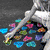 A hand pours colorful heart-shaped candies onto a dark surface, with blue, pink, and purple hearts scattered below.