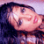 Pixelated close-up of a person with dark hair, light skin, and a pink mark on the cheek, set against a gradient background.