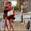 Two women embrace in a warm hug on a sunlit urban sidewalk, one holding a large red-and-white shopping bag.