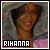 Pixelated image of a person with brown skin wearing gray hooded clothing and pink fabric, smiling with visible teeth.