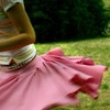 A person wearing a brown jacket and white striped shirt stands on grass with a pink skirt flowing outward.