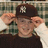 Pixelated image of a person wearing dark cap with white 'NY' logo, light brown hair visible under cap, dark shirt, and greenish background.