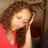 A pixelated image of a person with brown curly hair wearing a red top, holding their hand near their face in a contemplative pose.