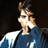 Pixelated static image of a person in profile wearing a blue and white shirt against dark background with visible dithering and compression artifacts.