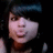 Pixelated close-up of a person with dark hair and light skin, wearing a dark top, against a black background with blue and white elements.
