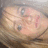 Pixelated image of a person with light skin tone lying down, wearing dark clothing and pink accessories on the face.