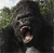 Static pixelated image of a large primate with dark fur, open mouth showing teeth and tongue, set against blurred green foliage background.