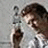 Pixelated static image of a person with brown hair wearing a white shirt, holding a dark object near their face against a light gray background.