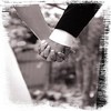 Two hands clasped in a handshake, one wearing a light sleeve and the other a dark sleeve, against a blurred background.