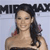 Pixelated image of a person with long dark hair wearing a strapless dark dress, standing against a light background with partial text above.