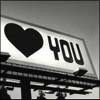 Black-and-white image of a heart symbol and the word YOU on a tilted rectangular background with blurred architectural elements below.