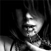 Black-and-white close-up of a person with long hair, multiple lip piercings, and layered necklaces, hand near chin.